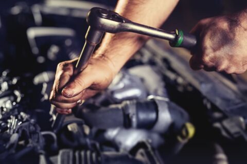Close-up of mechanic using socket wrench on diesel engine