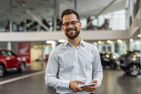 Smiling professional standing with a sleek car in showroom